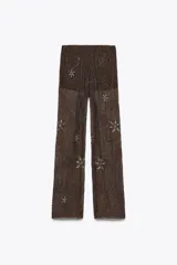Pantalón semitransparente color marrón chocolate, de tiro medio y corte recto. Presenta aplicación de abalorios y lentejuelas plateadas con motivos geométricos y florales. Incluye short interior a tono.