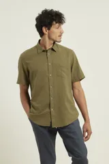 Camisa sport de manga corta color verde oliva, línea premium, con cuello clásico, cierre frontal con botones de coco y bolsillo de parche en el pecho. Confeccionada en lino y algodón.