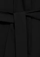 Mono negro con cuello camisero, sin mangas y cinturón tipo batín. Cierre delantero de botones oculto con tapeta y dos bolsillos laterales. Diseño recto y largo.