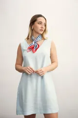 Vestido corto celeste de lino con cuello en V y costuras a la vista. Incluye pañuelo estampado con rayas y detalles en rojo.