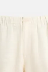Pantalón color crema de corte amplio, con cintura elástica ajustable con cordón, bolsillos laterales y trasero, cierre frontal con cremallera y botón.