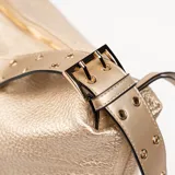 Bolso tipo hobo color beige con textura granulada y correa de hombro ajustable. Cierre superior con cremallera y tiras decorativas laterales con detalle de nudo.