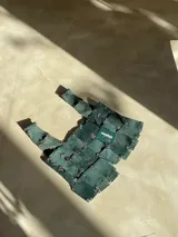 Top sin mangas de cuero genuino color verde inglés, con diseño de tiras entrecruzadas y unidas con herrajes metálicos, creando un efecto de malla o armadura.