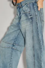 Jean de denim rígido azul claro, tiro medio-alto, con calce holgado y piernas anchas que se estrechan ligeramente hacia el tobillo. Presenta pinzas en la zona de las rodillas y un recorte en el lateral.