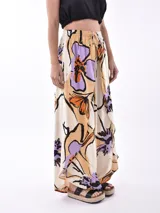 Pantalón palazzo de tela color crudo con estampado floral en tonos naranja, lila y negro.