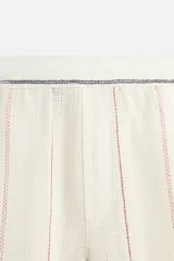Bermuda regular fit color crudo con rayas verticales en azul y rojo, confeccionada en tejido con mezcla de algodón. Cintura elástica ajustable con cordón interior. Bolsillos laterales y detalle de bolsillo trasero de plastrón.