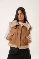 Chaleco color camel de cuero sintético con interior de piel sintética color crema, cierre frontal con cremallera y bolsillos laterales.