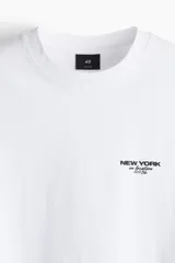 Remera blanca de corte holgado con cuello redondo y estampado pequeño con la frase "New York" en el pecho.