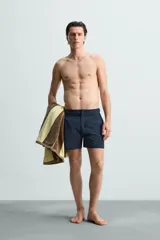 Short de baño celeste de tejido técnico con cintura elástica ajustable con cordón interior y trabillas laterales. Tiene bolsillos frontales y bolsillo trasero con cierre de cremallera. Cuenta con forro interior y cierre frontal con cremallera y botón a presión oculto.