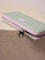 Billetera de poliuretano texturizado color rosado con cierre perimetral y logo metálico al frente.