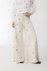 Pantalón de jean color crudo, corte wide leg, con bordados de cartas, dados y fichas de casino.
