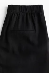 Pantalón negro de corte holgado, tiro alto con cintura elástica y piernas amplias. Confeccionado en tejido liviano de lino y viscosa. Presenta bolsillos al bies y bolsillos decorativos insertados atrás.