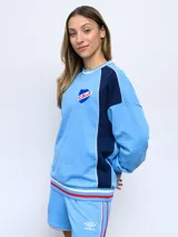 Buzo de felpa azul marino con mangas raglán rojas y detalles tricolor en puños, mangas y cuello. Incluye logo de Umbro bordado en el pecho y escudo del Club Nacional de Football.