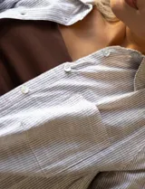 Camisa de manga larga a rayas verticales color beige y blanco, con cuello clásico, bolsillo en el pecho y cierre frontal con botones.