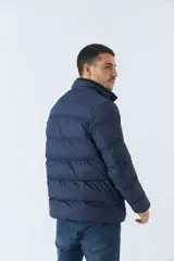 Campera inflada azul marino de nylon con cuello alto, cierre frontal con cremallera, bolsillos laterales con cierre y logo estampado en el pecho. El modelo usa talle M.