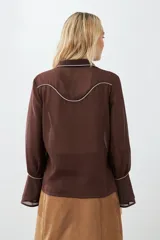 Camisa marrón de mangas largas con botones y detalles de pespuntes blancos en cuello, solapa y canesú.