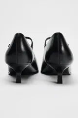Zapato de cuero negro con tacón kitten, tira delantera con hebilla ajustable y punta fina.