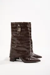 Bota de cuero color beige con punta fina, taco de 10cm y detalle de candado plateado en la caña.