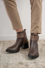 Bota corta de cuero marrón con puntera redondeada y taco cuadrado. Presenta una correa con hebilla alrededor del tobillo y cierre lateral.