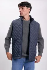 Chaleco azul marino con diseño acolchado de rombos, cuello alto y cierre frontal con cremallera. Tiene bolsillos laterales con ribete.