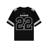 Camiseta negra de algodón con cuello redondo y mangas cortas. Presenta el logo de la marca Amiri en el pecho y el número 22 en la parte inferior. Diseño con llamas blancas en los hombros y rayas blancas en las mangas.