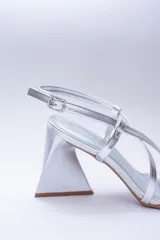 Sandalias de tacón alto color violeta metalizado, con tiras finas cruzadas en el empeine, puntera cuadrada y cierre con hebilla en el tobillo. El tacón es geométrico con forma de triángulo invertido.