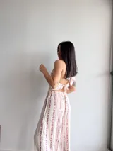 Pantalón ancho de tiro alto, color crema con estampado vertical de rayas irregulares en tono rosado/violeta. El pantalón tiene cintura elástica y corte recto y holgado.