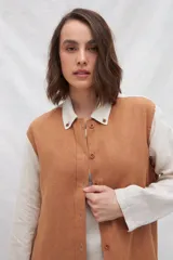 Camisa larga de lino color beige, con cuello camisero y cierre frontal con botones. Tiene mangas largas con puños abotonados, bolsillos laterales y una franja a contratono en la espalda y mangas.