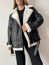 Campera gamulán negra con interior de corderito blanco. Incluye cinturón en la parte inferior, mangas y escote. Tiene bolsillos frontales.