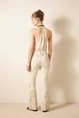 Pantalón de cuero ovino color crema con bordado de tachas metálicas y piedras en frente y espalda. De corte jeanero con calce flare, acceso delantero con botón metálico y cierre, bolsillos delanteros y traseros.