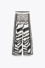 Pantalón de tiro medio con cintura elástica y pierna ancha. Presenta un estampado de líneas onduladas en blanco y negro, y aberturas laterales ajustables con lazadas.