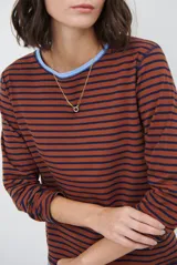 Remera de manga larga con diseño de rayas horizontales en azul y blanco, destacada por un cuello redondo en color bordó con costuras a la vista.