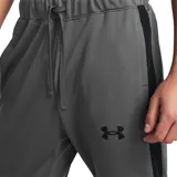 Conjunto deportivo Under Armour de hombre, color gris, compuesto por campera con cierre y pantalón largo. La campera tiene cuello alto, cierre frontal completo, bolsillos laterales y logo de la marca en el pecho. El pantalón tiene cintura elástica con cordón ajustable y logo de la marca en la pierna.