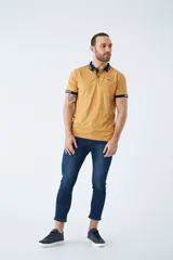 Remera tipo polo color ocre, de corte clásico, con cuello y mangas con terminaciones a contratono en azul marino y blanco.