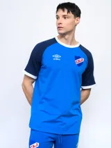 Remera de algodón azul con mangas ranglan azul marino y detalles en blanco en cuello y puños. Incluye logo de Umbro y escudo del Club Nacional de Football en el frente.
