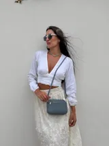 Bandolera pequeña de símil cuero color gris con textura granulada. Posee dos compartimientos principales con cierre y un bolsillo frontal con cremallera metálica. Incluye correa fina ajustable y extraíble.