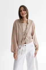 Camisa tostada en voile de algodón con cuello a la base y mangas balloon. Cierre frontal con lazos en la misma tela y tablas en el frente y en el medio en la espalda.