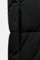 Chaleco largo negro acolchado con cuello alto ajustable con cordones y cierre frontal con cremallera.