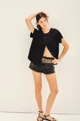 Camisa negra de manga corta con combinación de tejido de punto y plano, detalles de volados y frunces en pechera y espalda, acceso con botones fake nacar y medallita marcaria en espalda.