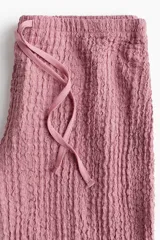 Pantalón recto color rosado, de punto con efecto arrugado, con elástico y cordón ajustable en la cintura.