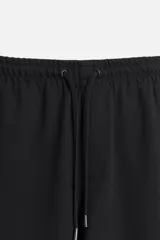Pantalón negro de corte cropped, con cintura elástica ajustable con cordón, bolsillos laterales y traseros de vivo. El bajo tiene terminación con vuelta.