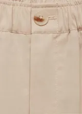 Pantalón de vestir color beige, de tiro alto, corte wide leg, con cintura elástica, pliegues frontales, cierre de cremallera y botón, y bolsillos laterales.