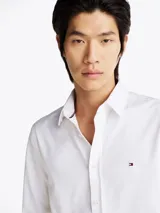 Camisa blanca de corte slim fit, con cuello abotonado, cierre con botones y logo de Tommy Hilfiger bordado en el pecho.