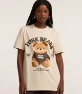 Remera color crema de algodón con cuello redondo y mangas cortas. Presenta un estampado de un oso de peluche con una sudadera que dice "New York" y la inscripción "York Bears".