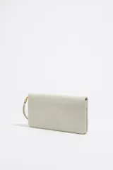 Billetera de cuero sintético color blanco con textura granulada. Tiene cierre con solapa y botón a presión, múltiples compartimentos internos para tarjetas y billetes, y un bolsillo con cierre para monedas. Incluye una correa de mano extraíble.