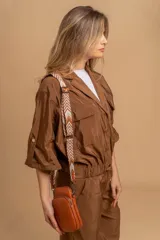 Bandolera pequeña tipo 'phone bag' de símil cuero color rosado pálido, con cierre de cremallera y correa ancha de tela con diseño de chevron en tonos claros.