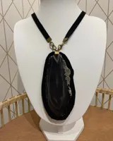 Collar con dije de piedra negra irregular con detalles en gris y blanco, montada sobre cuero negro y colgante de cinta de terciopelo negra con herrajes dorados.