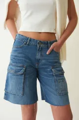 Bermuda de denim azul con tiro bajo, corte recto y largo hasta la rodilla. Presenta seis bolsillos, dos de ellos tipo cargo aplicados en el frente.