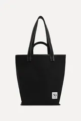 Bolso tipo tote confeccionado en algodón color negro, con doble asa y detalle de parche con el logo "50" y la leyenda "A Coruña".