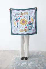 Pañuelo cuadrado de tela fina color celeste con estampado de motivos playeros y borde con diseño geométrico en tonos verde y rosa.